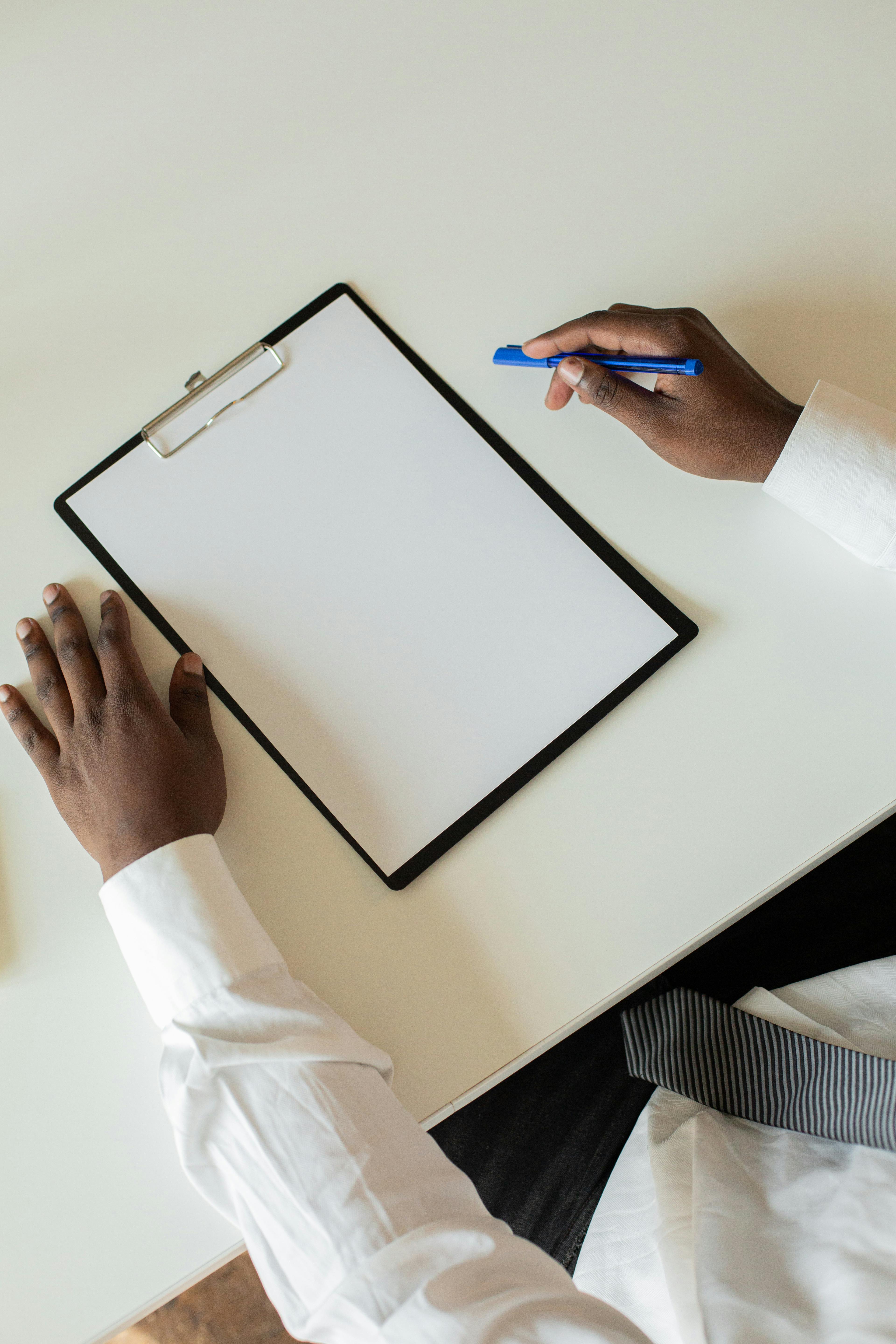 Person in business attire holding a pen and clipboard with blank paper, ready to take notes or start planning.